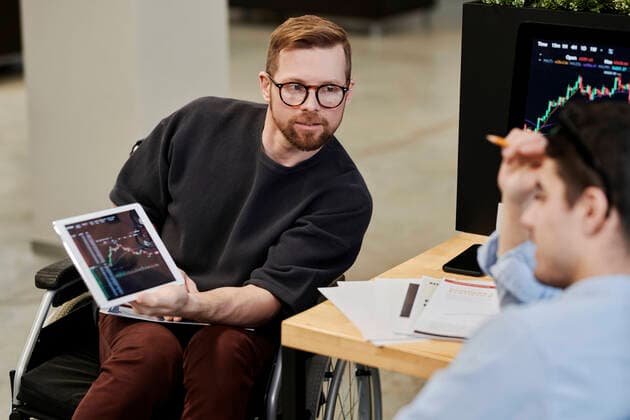 Disabled businessman showing cryptocurrency graph on tablet PC to colleague in office model released property released, DSHF00227