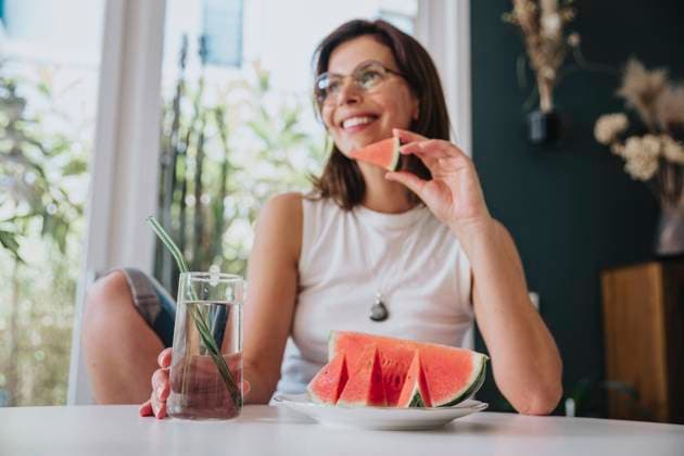 Woman sitting at home holding drinking glass by watermelon slice on table model released property released, MFF08845