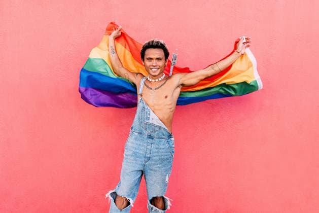 Creative Highlights Symbolbilder Happy guy waving rainbow lgbt flag against pink wall outdoors Copyright: xArtemxVarnitsinxArtemxVarnitsinx