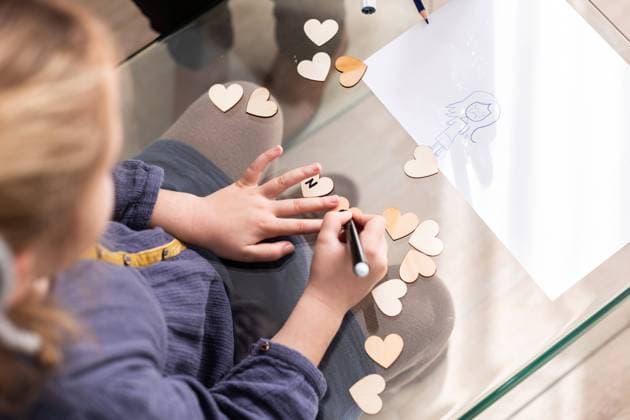 Top view of crop anonymous kid writing inscription on small hearts while sitting at glass table in room, Model released, Property released AngelSantamaria_PsychologicalHelp_45.jpg Copyright: xAngelxSantamariax MR