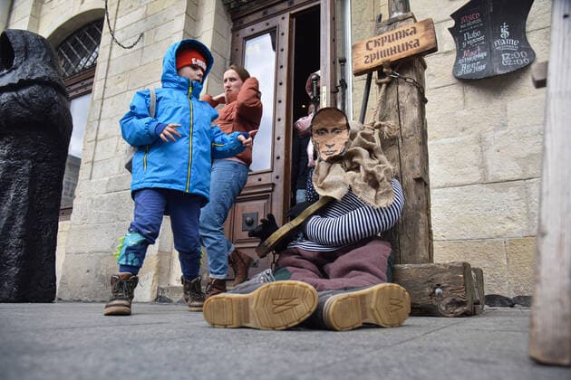 April 3, 2022, Lviv, Ukraine: A boy looks at a mannequin of a medieval prisoner with a portrait of Russian President Vladimir Putin at the entrance to a cafe. Due to Russia s military invasion of Ukraine, a mannequin of a medieval prisoner with the head of the occupying power, President Vladimir Putin, placed in medieval torture - the sinner s violin - was placed near Lviv cafe Lviv Ukraine - ZUMAs197 20220403_zaa_s197_403 Copyright: xPavloxPalamarchukx