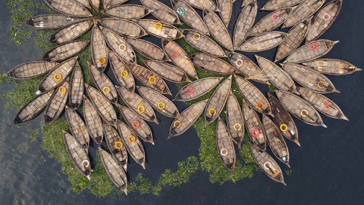 Creative Highlights World April 20, 2022, Dhaka, Dhaka, Bangladesh: Aerial view of Hundreds of wooden boats grouped fan out which look like the petals of a flower for a busy morning commute on Buriganga river in Dhaka. The boats, decorated with colourful patterned rugs, are ready to transport workers from the outskirts of the city to their jobs in the centre. The Buriganga river is used as a route into the densely populated Bangladeshi capital by millions of workers every day. On April 20, 2022 in Dhaka, Bangladesh. Dhaka Bangladesh - ZUMAe321 20220420_zia_e321_007 Copyright: xJoyxSahax xEyepixxGroupx