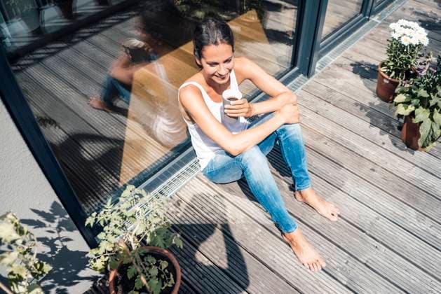 IMAGO Creative, Urban Lifestyle Happy woman with coffee cup sitting in balcony on sunny day model released, Symbolfoto property released, JOSEF07983