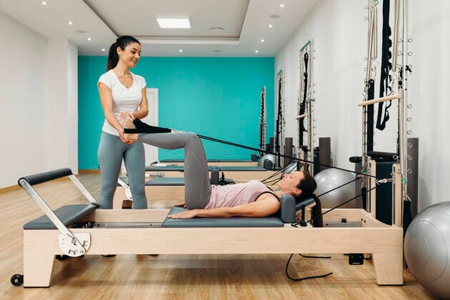 Smiling fitness instructor assisting woman doing pilates in studio model released, Symbolfoto property released, DMGF00676