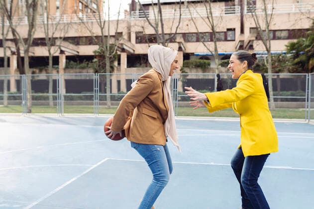 IMAGO Creative: Kollidierende Kulturen Cheerful businesswomen playing basketball at sports court model released, Symbolfoto, JCCMF05895