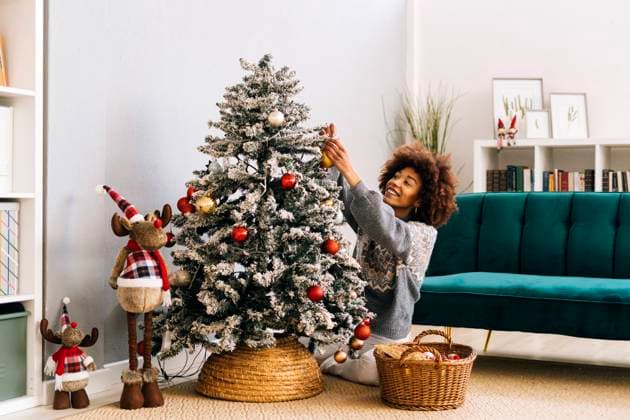 Happy woman decorating Christmas tree with bauble in living room at home model released, Symbolfoto property released, GIOF15278