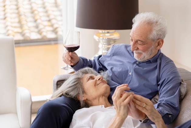 Smiling Senior woman lying on husband s lap sitting with wineglass on sofa at home model released, Symbolfoto property released, EIF03728