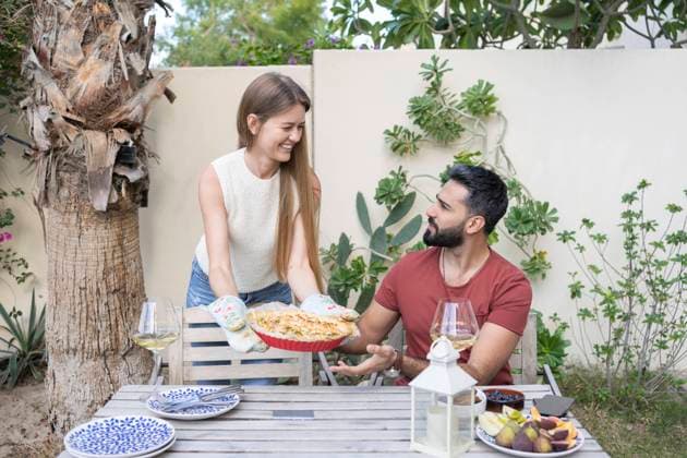 Happy woman showing homemade savory pie to man sitting at table in garden model released, Symbolfoto property released, SVKF00019