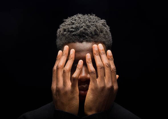 Head of upset black man with short curly hair covering face with hands on dark background in studio Copyright: xTxemaxGerardox Model Released