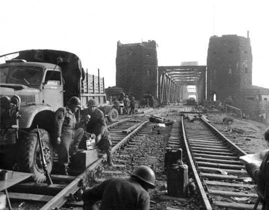 Two members of the U.S. Army record for broadcast purposes at Remagen (Germany) March 1945 Two members of the U.S. Army describe Flak cover and German planes diving for the Remagen bridge (background) on a recording designed for broadcast purposes in Germany, March 1945 Copyright: xPhoto12 Coll-DITE USISx DIT01138_235