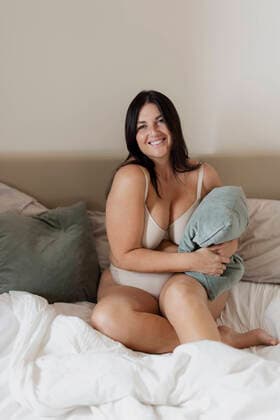 Creative Highlights Symbolbilder Smiling plus size woman holding pillow sitting on bed at home model released, Symbolfoto property released, EIF04038