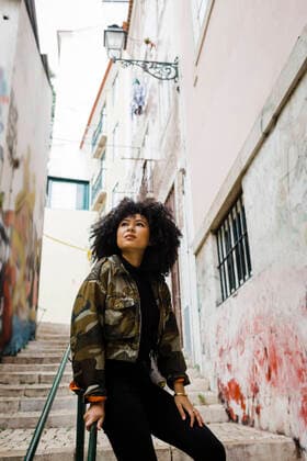 IMAGO Creative: Welttourismustag am 27. September IMAGO Creative: Nächste Generation, Sozial- und klimabewusst Young woman with curly hair sitting on railing model released, Symbolfoto, DCRF01129