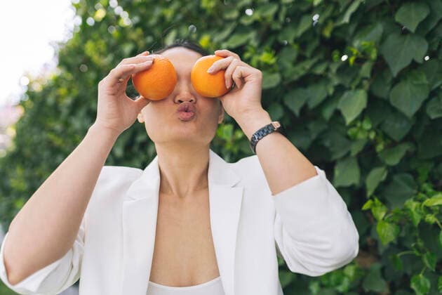 Creative Highlights Symbolbilder Woman with puckering lips holding oranges in front of eyes model released, Symbolfoto, JCCMF06189