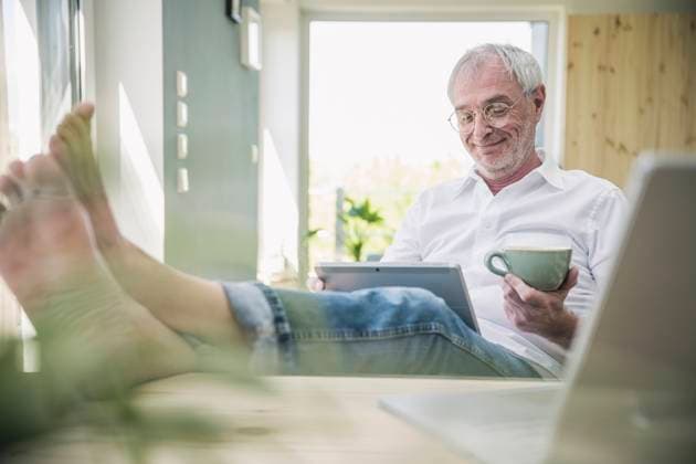 Smiling senior man with coffee cup using tablet PC sitting at home model released, Symbolfoto property released, UUF26119