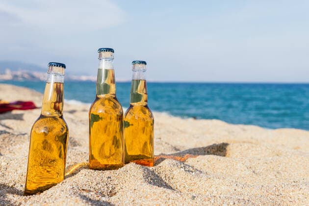 Glass bottles of cold beer placed on sand on blurred background of sea and blue sky on sunny day on resort Copyright: xDavidxMunozx Model Released