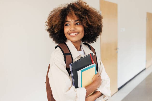 Creative Highlights Symbolbilder Smiling student with curly hair standing in corridor and looking away. Girl with textbooks and laptop in school. Copyright: xxArtemxVarnitsinx