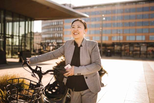 IMAGO Creative: Klimawandel - Klimabewusst Happy female professional wheeling bicycle on footpath during sunny day Sweden, Gothenburg, model released Copyright: xMaskotx , MA93950