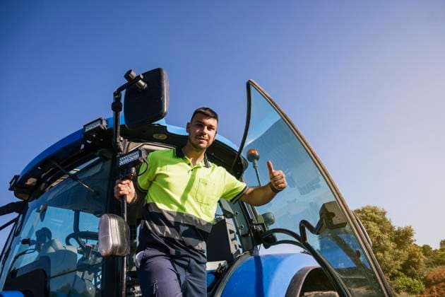 Young farmer gesturing thumbs up standing at door of tractor model released, Symbolfoto, JCMF02273