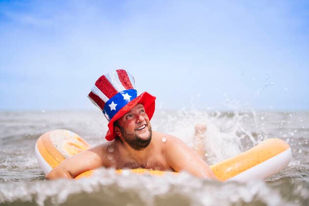 Creative Highlights Symbolbilder Carefree man wearing Uncle Sam hat swimming with pool raft in sea model released, Symbolfoto, OCMF02447