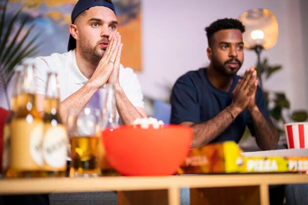 Curious young man wearing cap sitting by friend watching football match at home model released, Symbolfoto property released, Florence Florence Italy SBAF00147