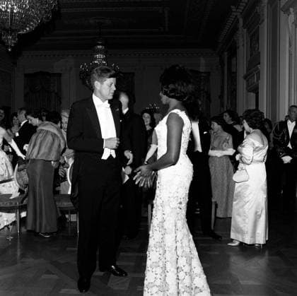 Dinner in honor of Vice President Lyndon B. Johnson (LBJ), Speaker of the House John W. McCormack, Chief Justice Earl Warren, 8:00PM. President John F. Kennedy talks with mezzo-soprano opera singer Grace Bumbry following Ms. Bumbrys performance at a dinner in honor of Vice President Lyndon B. Johnson, Speaker of the House of Representatives John W. McCormack, and Supreme Court Chief Justice Earl Warren. Harriet McCormack, wife of Speaker McCormack (back to camera), stands to the left of President Kennedy; Ruth Ribicoff, wife of Secretary of Health, Education and Welfare Abraham Ribicoff (in back), stands at far right. East Room, White House, Washington, D.C. Copyright: xpiemagsx