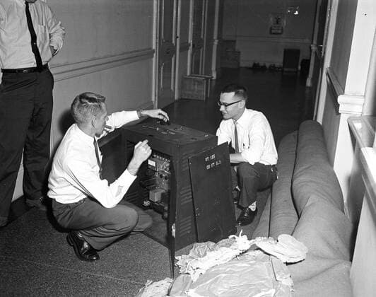 Trip to Europe: Arrival in Vienna, Austria 10:50AM; White House Army Signal Agency (WHASA) staff in Vienna. Three unidentified men (two kneeling and one standing) prepare White House Army Signal Agency (WHASA) equipment for a summit between President John F. Kennedy and Soviet Union Premier Nikita Khrushchev in Vienna, Austria. The man in the middle kneeling is smoking a cigar. Copyright: xpiemagsx