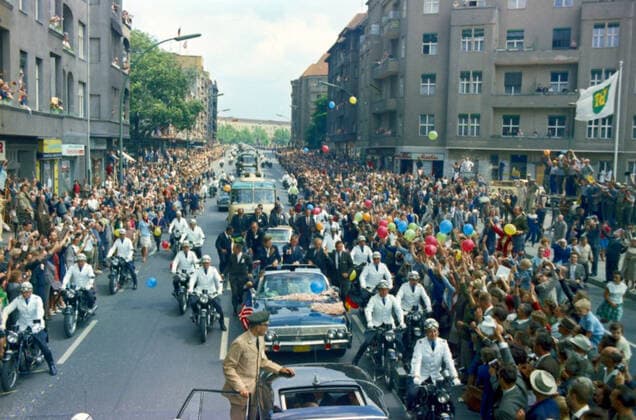 Trip to Europe: Germany, West Berlin: President Kennedy in motorcade with Willie Brandt, Mayor of West Berlin and Konrad Adenauer, Chancellor of West Germany. President John F. Kennedy (standing in second car) waves to crowds from the Presidential limousine (Lincoln-Mercury Continental convertible) as his motorcade travels through West Berlin, West Germany (Federal Republic). Standing with the President: Mayor of West Berlin, Willy Brandt; Chancellor of West Germany, Konrad Adenauer. Also pictured: Special Assistants to President Kennedy, Kenneth P. O Donnell and David F. Powers; Director of the United States Secret Service, James J. Rowley; White House Secret Service agents, Jerry Blaine, Sam Sulliman, Floyd Boring, Roy Kellerman, and Paul Copyright: xpiemagsx