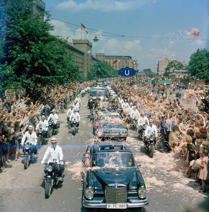 Trip to Europe: Germany, West Berlin: President Kennedy in motorcade with Willie Brandt, Mayor of West Berlin and Konrad Adenauer, Chancellor of West Germany. President John F. Kennedy (in second car, mostly hidden) stands in the Presidential limousine (Lincoln-Mercury Continental convertible) as his motorcade travels through West Berlin, West Germany (Federal Republic). Standing with the President: Mayor of West Berlin, Willy Brandt; Chancellor of West Germany, Konrad Adenauer. Also pictured: Special Assistant to President Kennedy, Dave Powers; Director of the United States Secret Service, James J. Rowley; White House Secret Service agents, Floyd Boring, Jerry Blaine, and Roy Kellerman. Crowds line the street, throwing confetti. Blue stre Copyright: xpiemagsx
