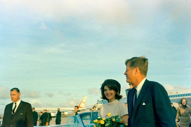 Trip to Texas: Houston: Arrival at Houston International Airport. President John F. Kennedy (right) and First Lady Jacqueline Kennedy (holding bouquet of yellow roses) arrive at Houston International Airport in Houston, Texas; Air Force One is visible in the background. Also pictured: White House Secret Service agents, Roy Kellerman and Clint Hill. Copyright: xpiemagsx