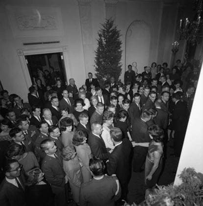 White House Staff Christmas Party in the East Room, 6:30PM. President John F. Kennedy and First Lady Jacqueline Kennedy (both in center right foreground, seen from above) greet guests gathered in Cross Hall, during a Christmas party for White House staff; guests fill the hallway and into the Green Room at left. Also pictured: Air Force Aide to the President, Brigadier General Godfrey T. McHugh; White House Secret Service agent, Clint Hill. White House, Washington, D.C. Copyright: xpiemagsx