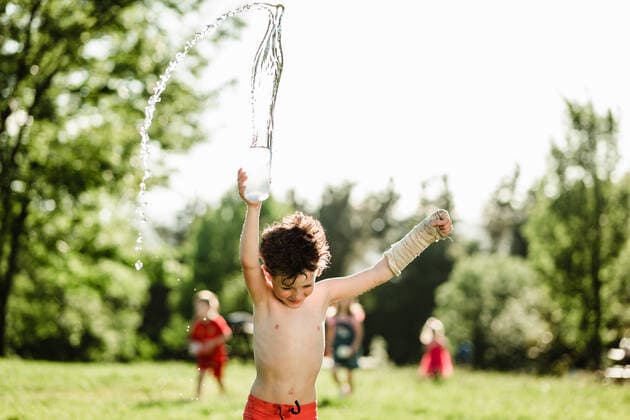 IMAGO Creative: Sommer, Sommertage im Garten Young shirtless boy in shorts and casted arm splashing water while standing in green park on sunny day in summer, Model released HodeiUnzueta_HotSummer_00024.jpg Copyright: xHodeixUnzuetax MR