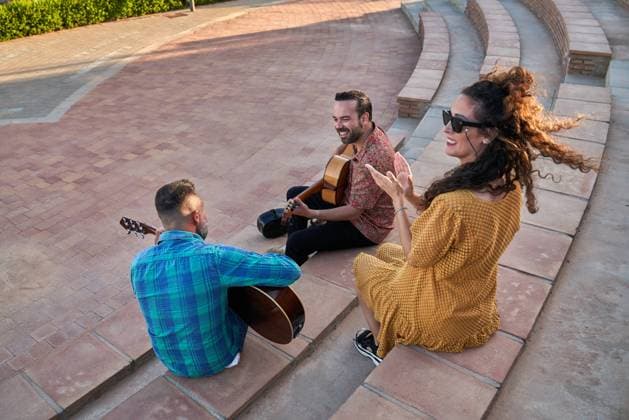 IMAGO Creative: Lokalhelden - Kunst und Kultur From above full body of content male musicians playing songs on acoustic guitars and looking at each other while sitting on steps with cheerful woman on street, Model released JavierBermudez_RubenGuitarrist_28.jpg Copyright: xJavierxBermudezx MR