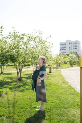 IMAGO Creative: Sommer, Sommertage im Stadtpark Smiling mother carrying her baby in a shawl sling at city park, Model released LiliyaSolopova_MumsWithBabiesOutdoors_00003.jpg Copyright: xLiliyaxSolopovax MR