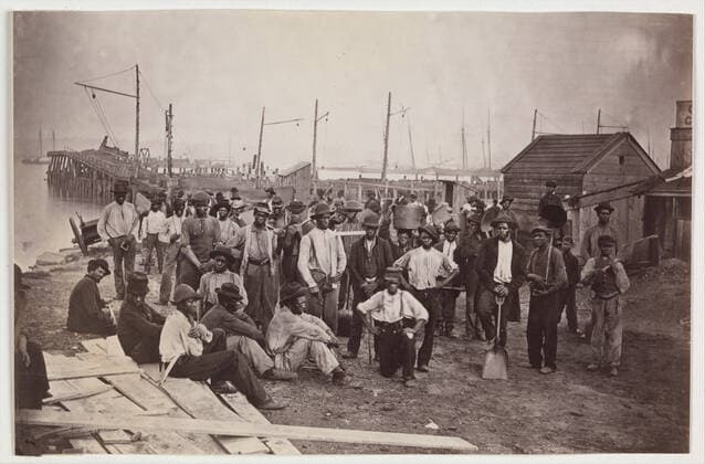 Laborers at Quartermaster s Wharf, Alexandria, Virginia 1863 65 Attributed to Andrew Joseph Russell American The United States Quartermaster™s office managed the supply, warehousing, and distribution of food, fuel, ordnance, medical supplies, forage for animals, and even mail delivery for the army. This extraordinary view shows a group of emancipated slaves who worked as paid laborers for the army along the immense set of wharves at Alexandria, Virginia. One of the freedmen holds a carpenter™s square, one a barrel, the others coal shovels marked with United States Army initials. The workers moved commodities either into storage or onto wagons or railroad cars to be taken to the front.. Laborers at Quartermaster s Wharf, Alexandria, Vi Copyright: xpiemagsx Metbot-34774
