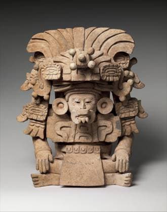 IMAGO Cultures of the world, Zapotec Kultur in Mexiko Funerary Urn with Deity ca. 6th century Monte Alban A seated figure forms the body of this effigy funerary urn, created in the style associated with the Zapotec site of Monte Alban in the southern Mexican state of Oaxaca. The individual, perhaps a deity or a human impersonating a god, rests his hands on his knees and leans slightly forward. The stoic gaze of the figure is interrupted by a large buccal mask that protrudes from his mouth, including three sharp fangs. Spiral-shaped elements incised on either side of each eye might represent tattoos or scarification. The head is accented with red pigment, suggesting that the figure would have once been brightly painted. He also wears large round earflares, a wide pectoral with hieroglyphic ele Copyright: xpiemagsx Metbot-51518