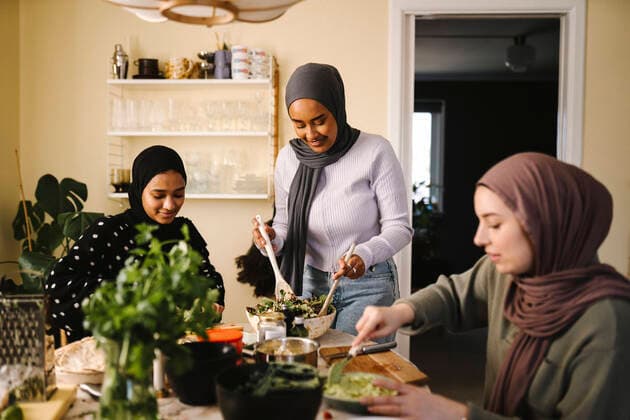 Smiling woman making salad while standing by friends preparing food at table in kitchen Sweden, Gothenburg, model released, property released Copyright: xMaskotx , MA93290 MA93290