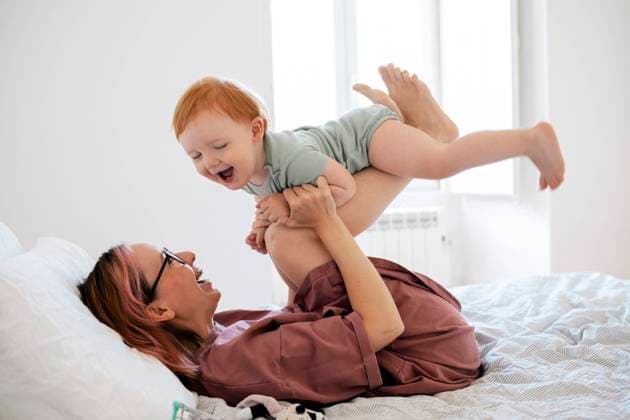 Creative Highlights Symbolbilder Cheerful mother picking baby boy while lying on bed in bedroom Portugal, Lisbon, model released, property released Copyright: xMaskotx , MA94435 MA94435