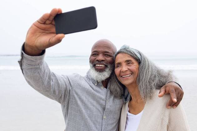 Creative Highlights Symbolbilder Couple taking a picture with smartphone at the beach Front view of happy senior African-American couple taking a selfie while standing on the beach with mountains in the background. Authentic Senior Retired Life Concept, model released, , property released, Cape Town, South Africa, 19.03.2019, 1262790.jpg, senior life, active seniors, retirement, lifestyle, leisure, photographing, taking, picture, digital camera, photo, photography, smartphone, mobile phone, wireless technology, phone, holding, showing, screen, touching, coastline, shore, ocean, sea, beach, waves, water, sunny, sand bright, vacation, summertime, holidays, blue, sky, sunlight, clear, sunshine, sun, clouds, cloud, skies, cloudy, outdoor, day, nature, weather, bright, light,