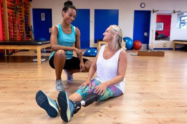 IMAGO Creative: Gesundheit, Prothese Female trainer talking with disabled active senior woman in sports center Front view of African-american female trainer talking with disabled Caucasian active senior woman in sports center. Sports Rehab Centre with physiotherapists and patients working together towards healing, model released, , property released, Cape Town, South Africa, 24.03.2019, 1273248.jpg, millennial, beautiful, senior citizen, aged, ageing process, retired, retirement, pensioner, active senior, active, senior, disabled, handicapped, physical impairment, sportswear, leg, prosthetic leg, artificial, artificial leg, gym, fitness center, sports center, floor, sitting, crouching, talking, interacting, smiling, happy, cheerful, motivation, dedication, determination, hobb