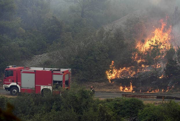 PXL_Zaton fire by the road Fire in an open area near the Zaton site in the Vodice hinterland, Croatia on July 13, 2022. About 30 firefighters with a dozen vehicles are on the ground, and two Canadairs joined the ground forces in extinguishing the fire. There are pine forests above, low vegetation, and endangered buildings. HrvojexJelavic PIXSELL