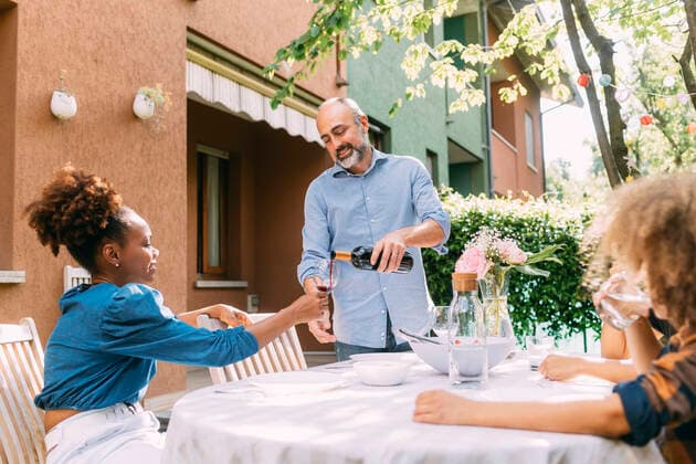 Man pouring wine into glass for woman sitting at dining table in backyard model released, Symbolfoto property released, MEUF06395
