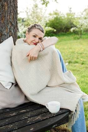 IMAGO Creative: Gesundheit, Stille IMAGO Creative: Jahreszeit Frühling, Frühlingsanfang am 20. März Woman wrapped in blanket sitting with coffee cup on bench by tree trunk model released, Symbolfoto property released, LLUF00708