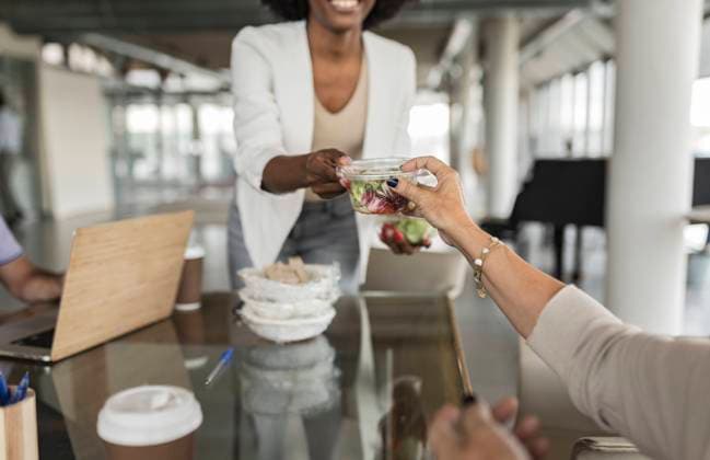 Businesswoman giving salad box to senior colleague at desk model released, Symbolfoto property released, JCICF00179