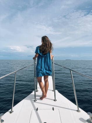 Creative Highlights Symbolbilder Back view of young woman in blue dress standing on a bow of a yacht Copyright: xArtemxVarnitsinxArtemxVarnitsinx