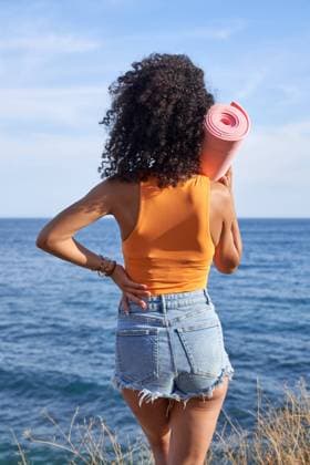 Creative Highlights Symbolbilder Back view of Hispanic female with rolled yoga mat while standing on coast near waving sea in coastal area, Model released JavierBermudez_SanaBeach_00008.jpg Copyright: xJavierxBermudezx MR