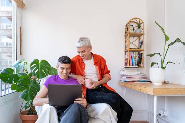 Creative Highlights Symbolbilder Smiling gay couple using laptop sitting on armchair at home, Model released JordiBataller_QueerReality_129.jpg Copyright: xJordixBatallerx MR