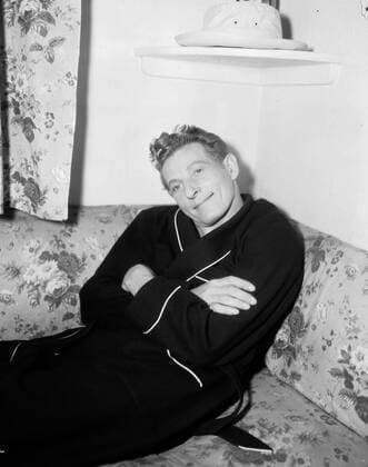 Circa 1965, London, England, United Kingdom: American actor DANNY KAYE sitting on a floral couch wearing a dressing gown. London United Kingdom - ZUMAk09_ 19650402_zka_k09_879 Copyright: xKeystonexUSAx