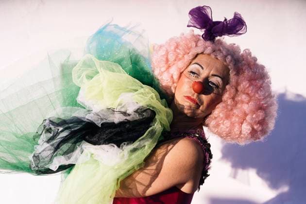 Side view of sad mature female clown in curly pink wig with bright makeup carrying pile of tutu skirts and looking away after performance on street on sunny day JavierBallester_GiraGiraClown_25.jpg Copyright: xJavierxBallesterx Model Released