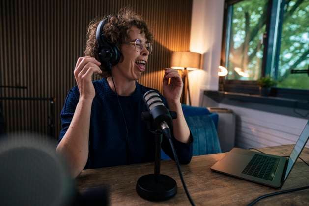 Presenter wearing headset making face sitting with microphone and laptop at desk in recording studio model released, Symbolfoto property released, JOSEF11216