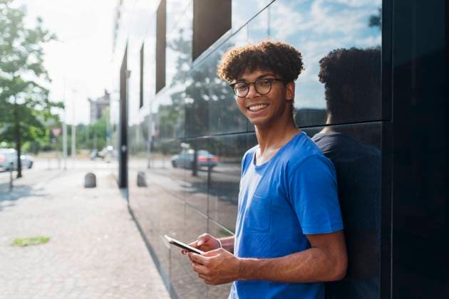Smiling young man using mobile phone leaning on wall model released, Symbolfoto, MEUF07673